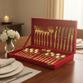 Set of gold cutlery in a red box on a dining table with white flowers and plates.